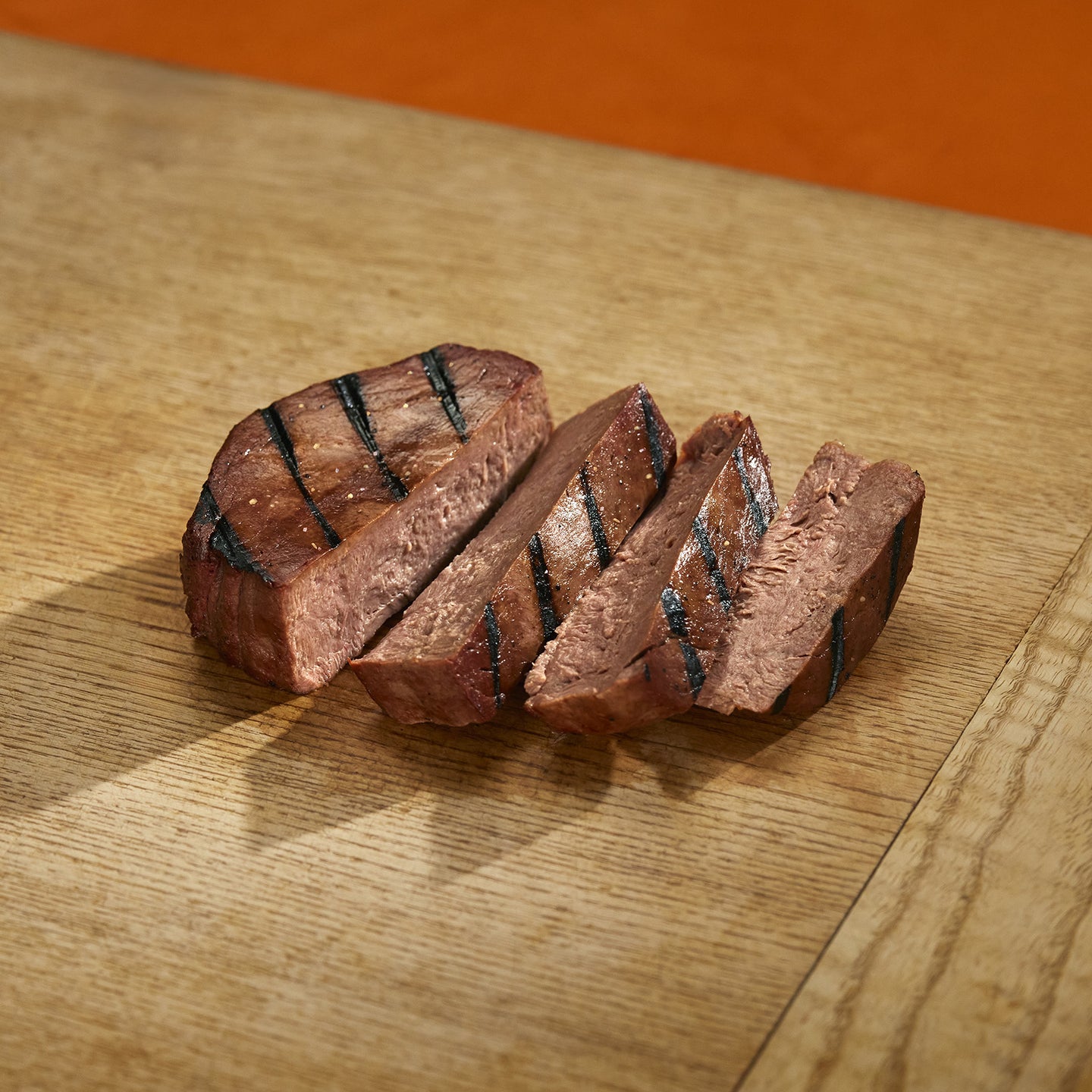 Sliced grilled steak on a wooden cutting board with an orange background